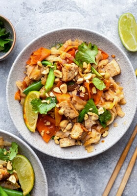 A serving of vegan pad thai in a white bowl with chopsticks on the side