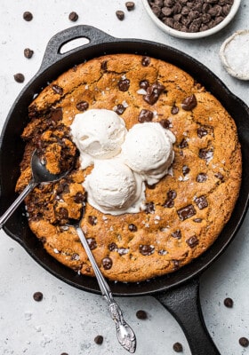 A giant chocolate chip cookie inside of a cast-iron skillet with scoops of dairy-free vanilla ice cream on top