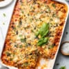 A rectangle baking casserole of zucchini lasagna with a missing square topped with basil and cheese