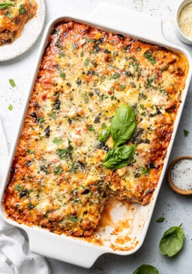 A rectangle baking casserole of zucchini lasagna with a missing square topped with basil and cheese