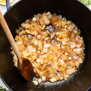 Sautéed onions in a blue dutch oven / pot with a wooden spoon