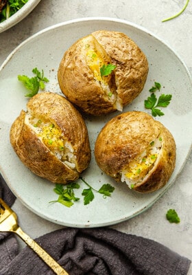 Three perfect air fryer baked potatoes with vegan butter and parsley on a white plate