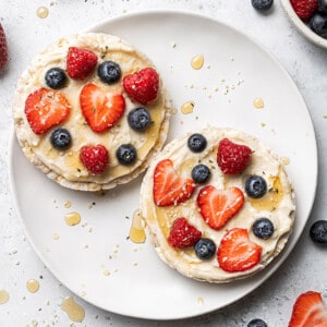 Two loaded rice cakes topped with cream cheese and berries on a white plate