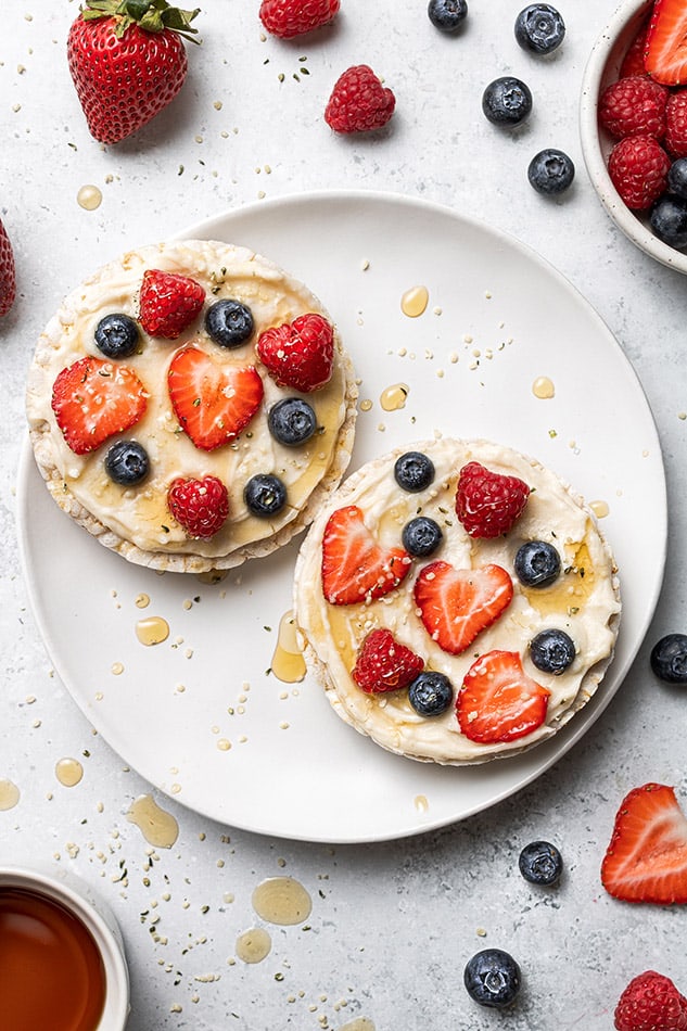 Two loaded rice cakes topped with cream cheese and berries on a white plate