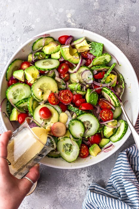Overhead view of a bowl of Cucumber Tomato Salad with dressing being poured on