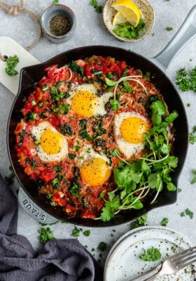 Top view of healthy shakshuka in a grey cast-iron skillet with micro-greens on a grey background