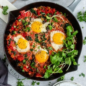 Top view of healthy shakshuka in a grey cast-iron skillet with micro-greens on a grey background