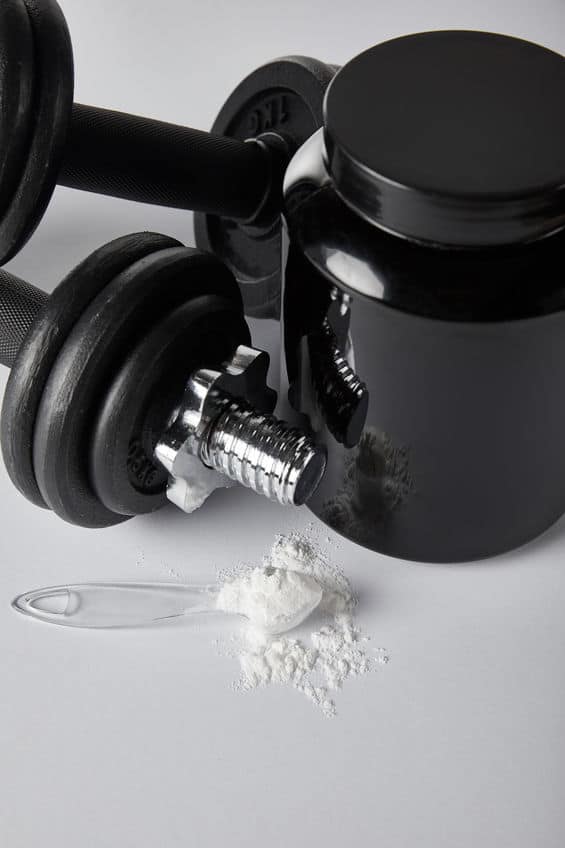 jar near dumbbells and spoon with protein powder on white