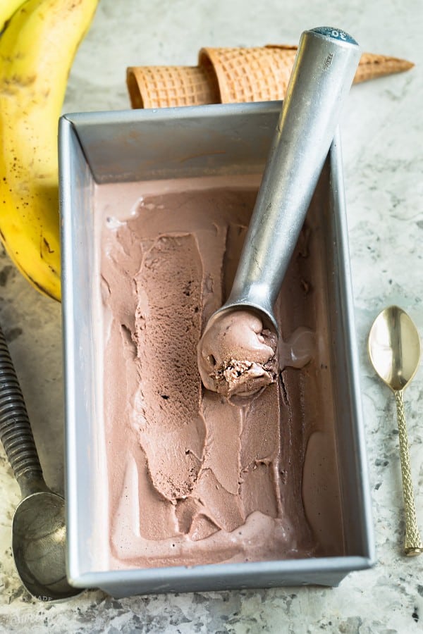 Overhead image of two ingredient chocolate banana ice cream in silver container with ice cream spoon and fresh banana.