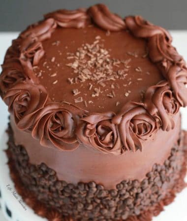 Ultimate Triple Chocolate Layer Cake - The best triple layer chocolate cake with the easiest milk chocolate frosting covered with mini chocolate chips on a white cake platter.