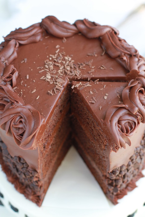 Cut out slice of simple Triple Chocolate Layer Cake with milk chocolate frosting and chocolate chips on a cake plate.