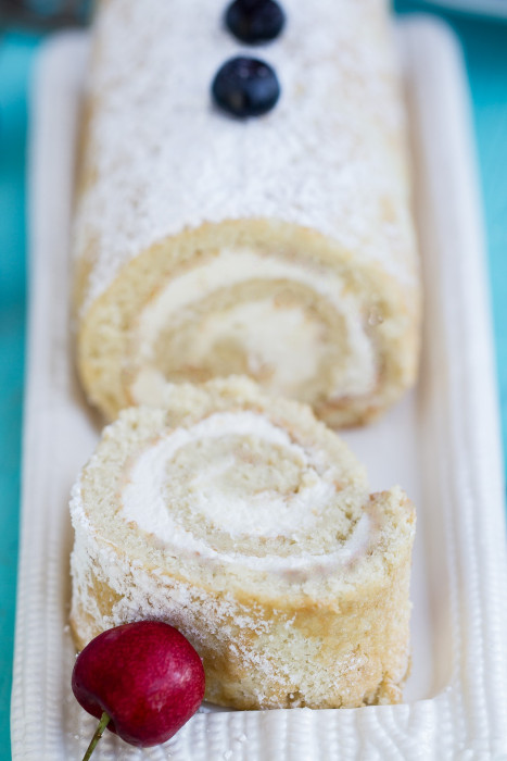 Vanilla cake roll on a platter with a slice cut