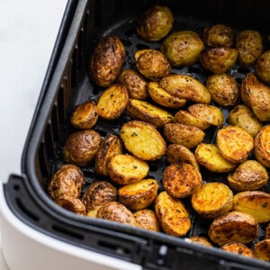 Crispy roasted potatoes inside of an Air Fryer basket with a kitchen towel beside it
