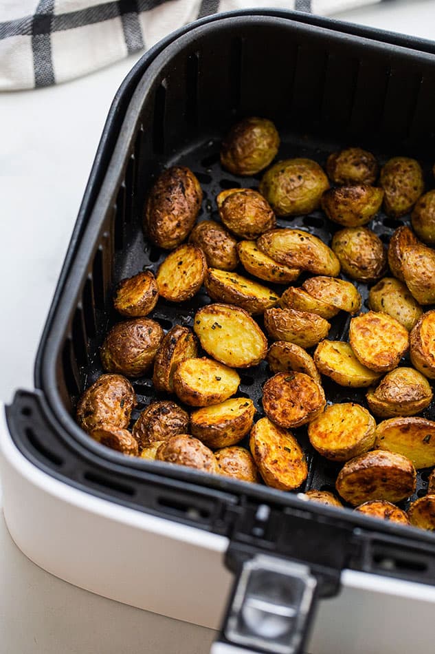Crispy roasted potatoes inside of an Air Fryer basket with a kitchen towel beside it