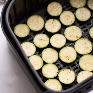 Uncooked zucchini slices inside of an Air Fryer basket on a countertop