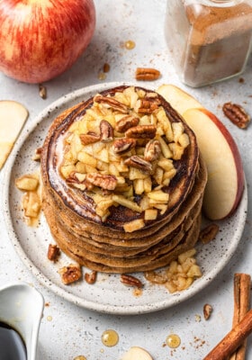 Overhead view of a stack of apple pancakes topped with chopped apples and pecans
