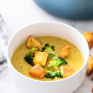 A serving of vegan broccoli cheddar soup topped with crispy croutons in a white bowl