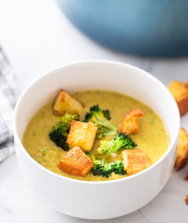 A serving of vegan broccoli cheddar soup topped with crispy croutons in a white bowl