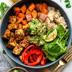 Top view of a vegan burrito bowl on a grey background with a gold fork