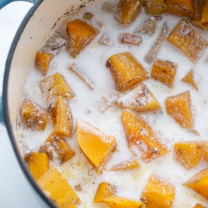 Cooked butternut squash cubes, chopped carrots, chopped apples and coconut milk in a blue dutch oven pot with