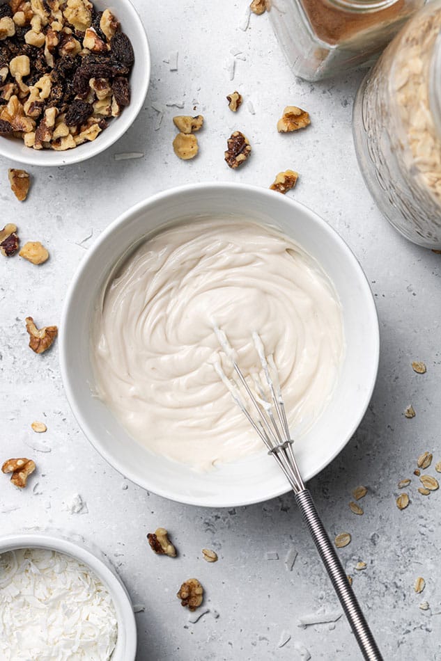 Dairy-free and vegan cream cheese glaze in a bowl with a small metal whisk
