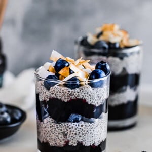 Side view of two paleo chia pudding in a cup layered with blueberries and blueberry jam with coconut chips