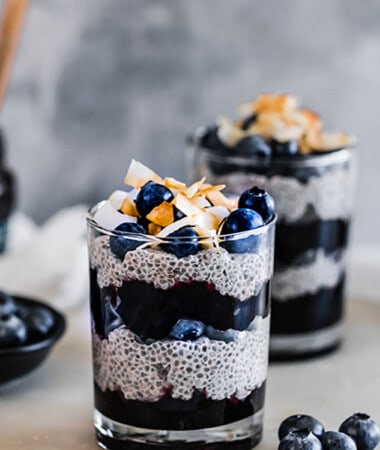 Side view of two paleo chia pudding in a cup layered with blueberries and blueberry jam with coconut chips