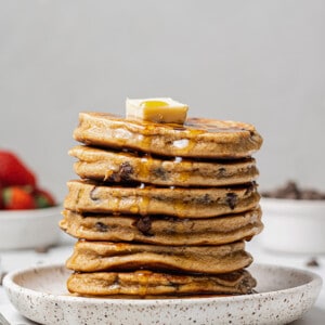 Side shot of a stack of chocolate chip pancakes with maple syrup on a white plate