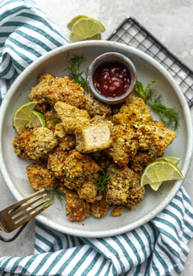 A bowl with tofu nuggets, lime and ketchup