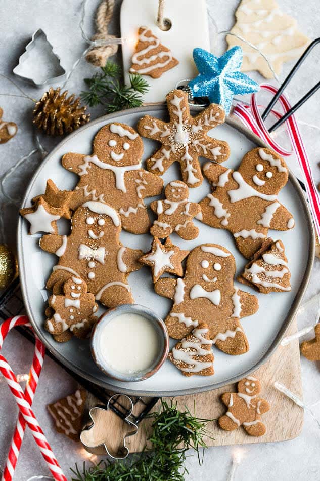 Top view of decorated vegan gingerbread cookies in a grey plate on a grey background with a vegan royal icing bowl