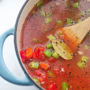 Vegetable broth, diced tomatoes, carrots, a bay leaf simmering in a blue pot
