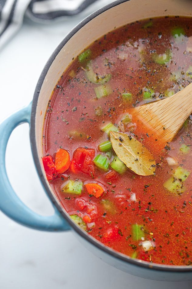 Vegetable broth, diced tomatoes, carrots, a bay leaf simmering in a blue pot