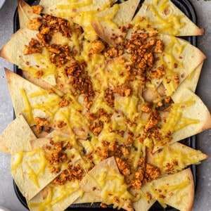 Baked grain-free tortilla chips topped with melty vegan cheese and a savory tofu crumble