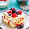 Side view of one slice of icebox cake on a white plate with a fork and mixed berries