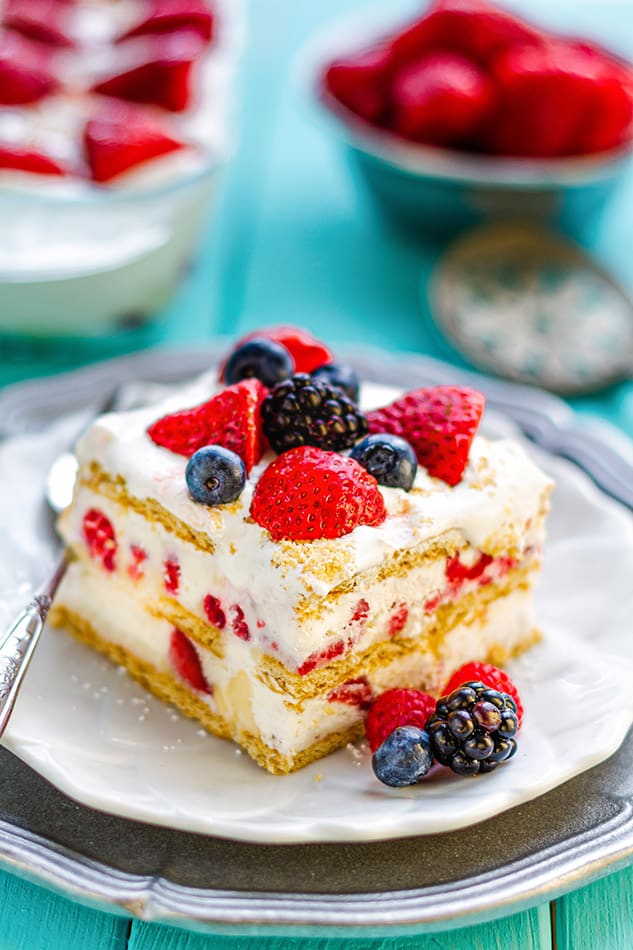 Side view of one slice of icebox cake on a white plate with a fork and mixed berries