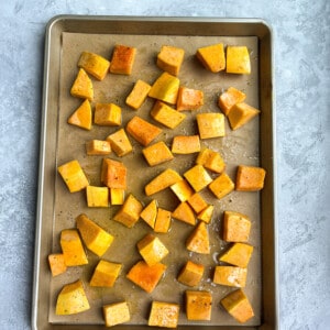 Top view of raw butternut squash cubes on a line baking sheet