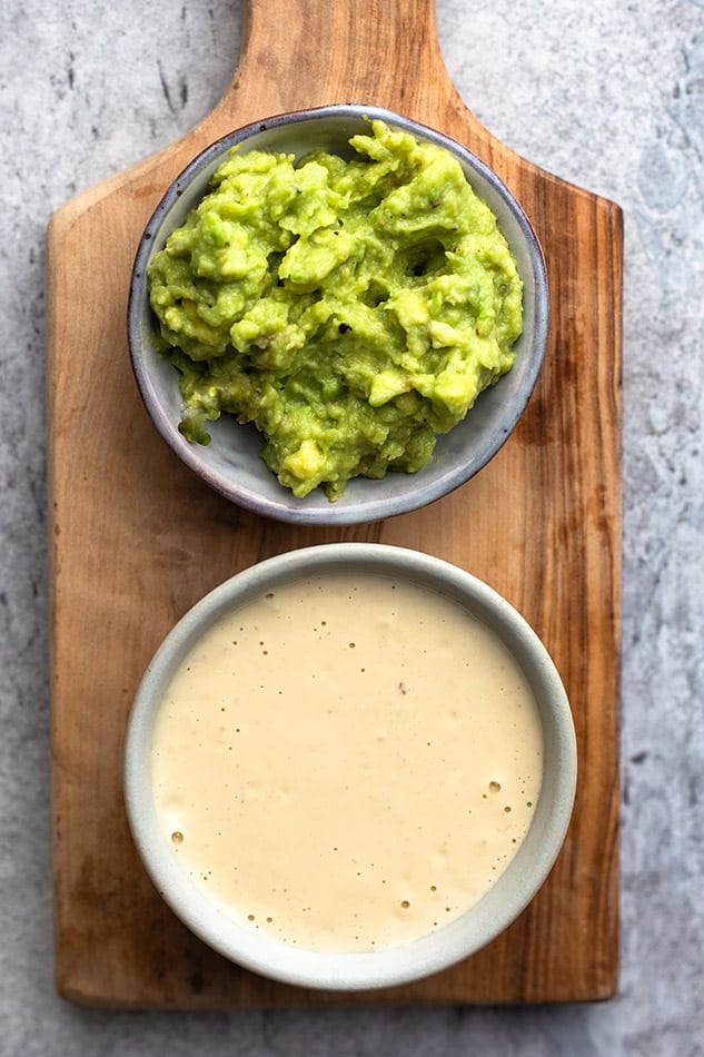 Top view of avocado dip and cashew dip for sweet potato fries on top of a wooden cutting board