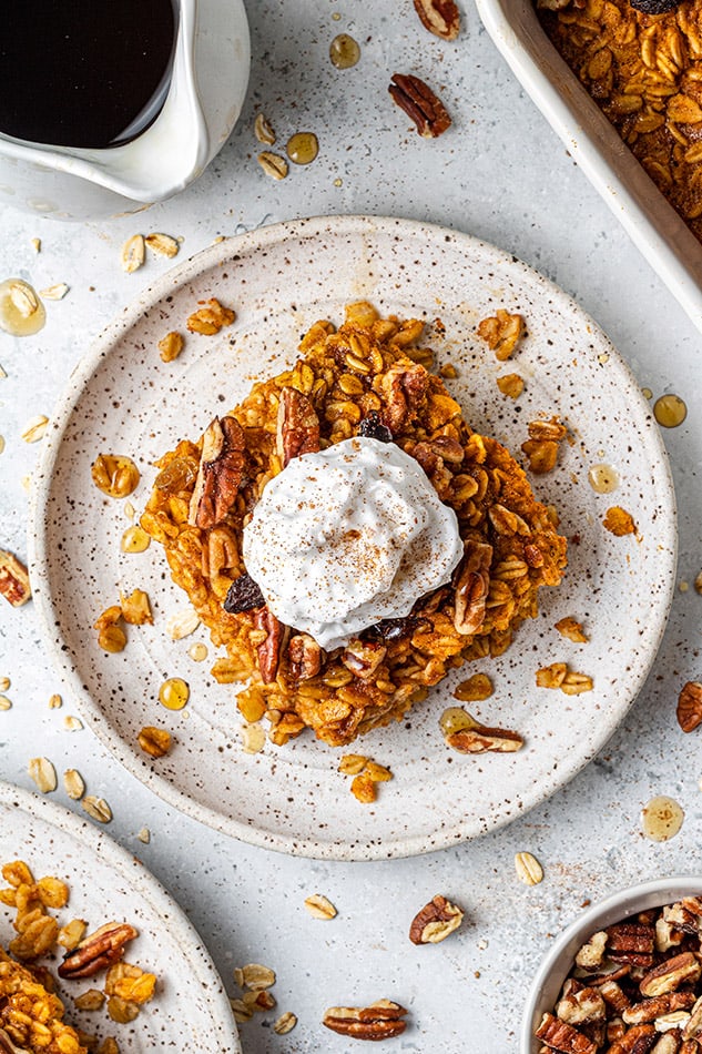 A slice of pumpkin baked oatmeal on a plate beside a bowl of chopped pecans