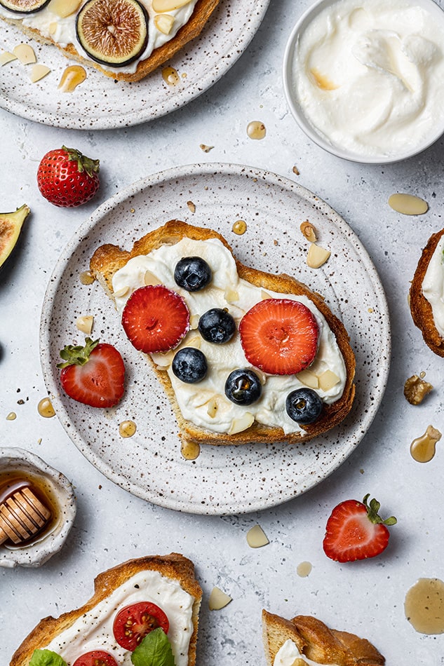 One slice of whipped ricotta toast on a speckled plate with blueberries and strawberry slices on top