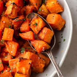 Close-up shot of roasted sweet potatoes in an oval bowl with a spoon