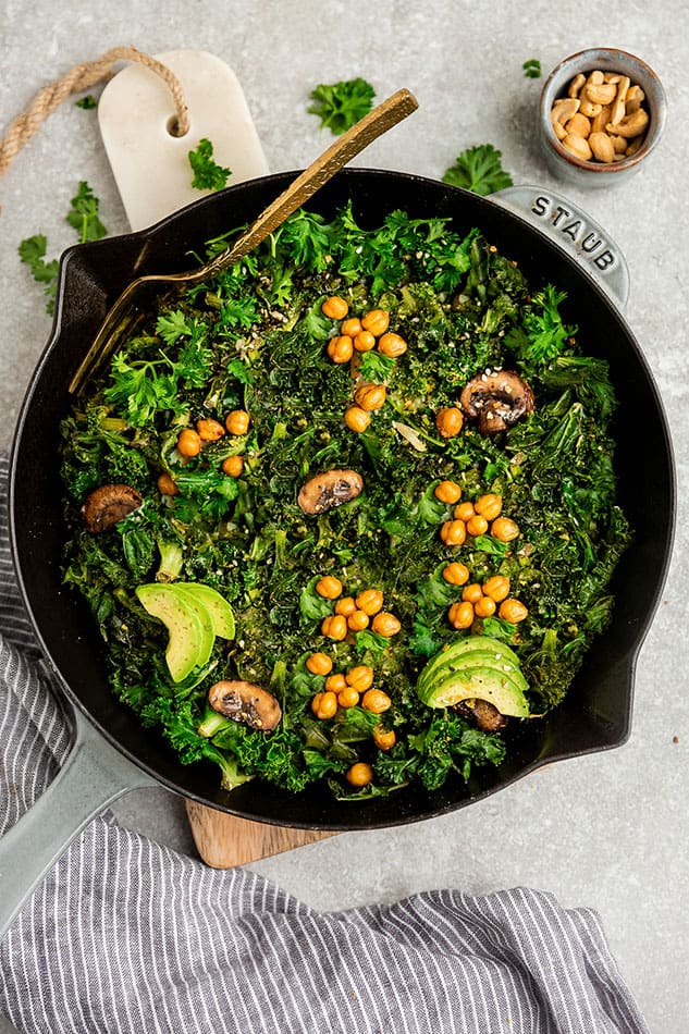 Top view of vegan green shakshuka in a grey cast-iron skillet on a grey background with a gold fork