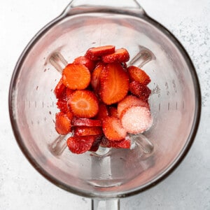 Top view of sliced strawberries, maple syrup, apple cider vinegar, oil and salt in a blender