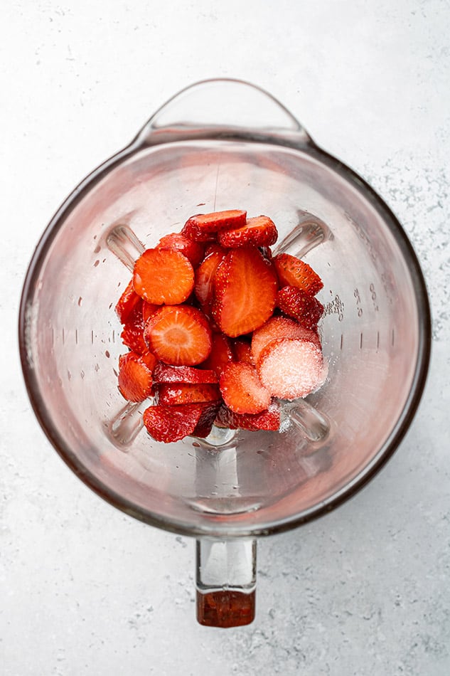 Top view of sliced strawberries, maple syrup, apple cider vinegar, oil and salt in a blender