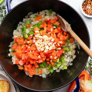 Chopped bell peppers, garlic and onions in a blue dutch oven / pot with a wooden spoon