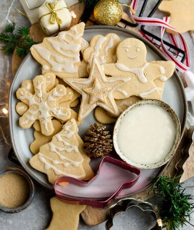 Top view of decorated vegan sugar cookies in a grey plate on a grey background with a vegan royal icing bowl