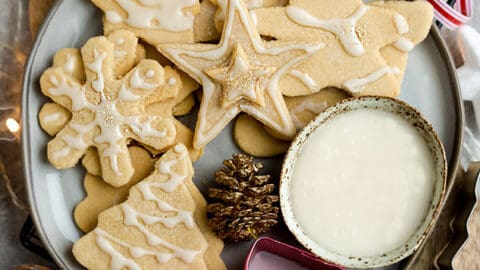 Top view of decorated vegan sugar cookies in a grey plate on a grey background with a vegan royal icing bowl