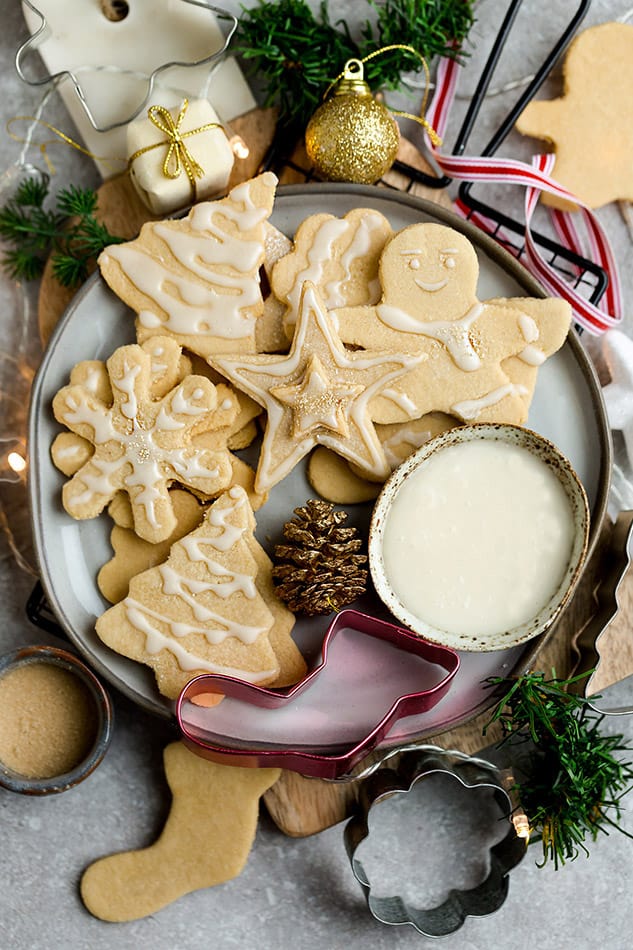 Top view of decorated vegan sugar cookies in a grey plate on a grey background with a vegan royal icing bowl