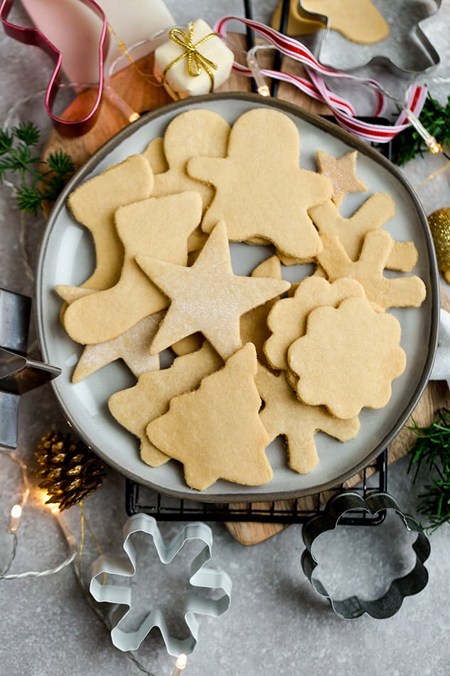 A plate of undecorated sugar cookies next to cookie cutters and a pinecone