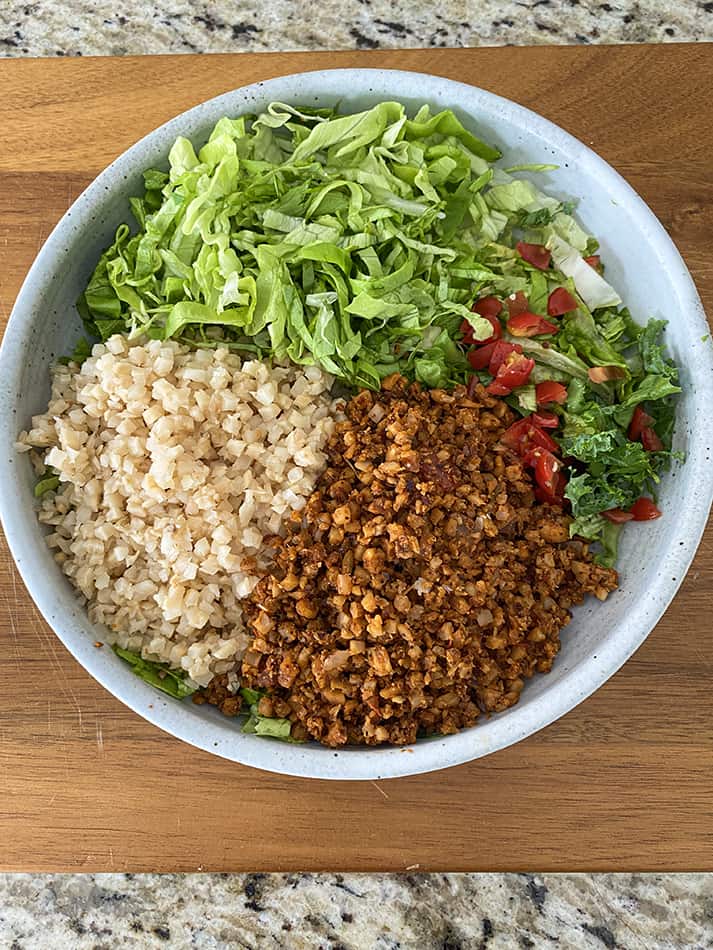 A large bowl containing shredded lettuce, cauliflower rice, pico de gallo and a walnut taco filling