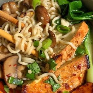 Top view of a bowl of miso ramen with chopsticks topped with tofu, bok choy and mushrooms.